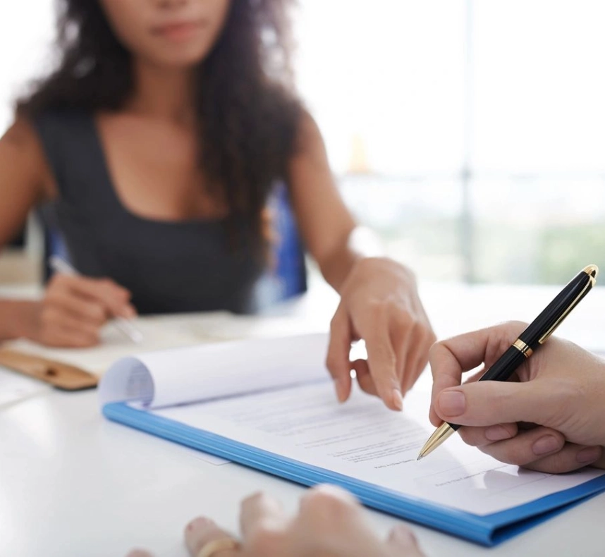 A woman is writing on paper with another person in the background.