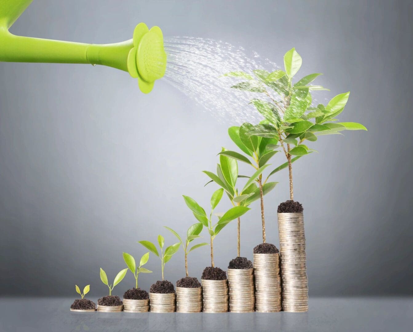 A watering can spraying water on plants growing from stacks of coins.